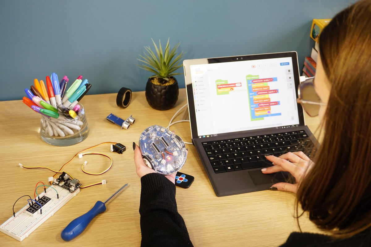 Une ado programme son robot en blocs à son bureau, le robot dans la main