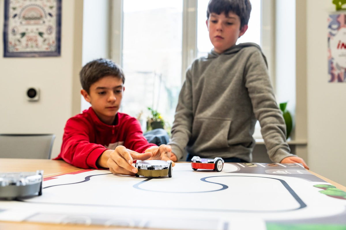 Deux enfants font rouler leurs robots sur un parcours pendant un atelier de robotique