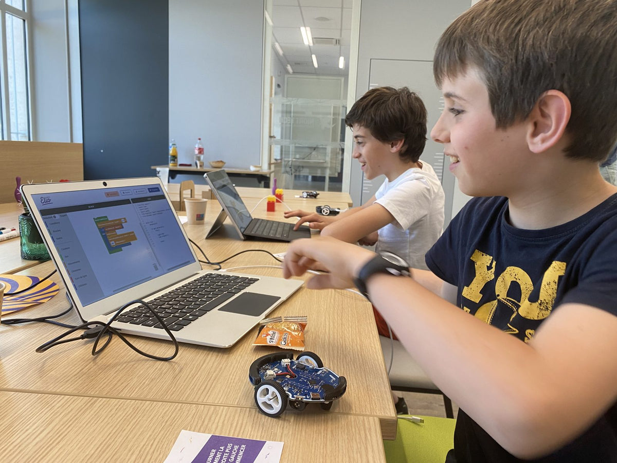 Deux enfants souriants programment leur robot en blocs sur ordinateur