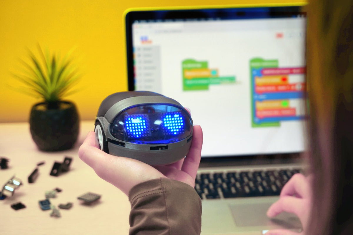Robot Eliobot aux yeux LED en forme de cœur, tenu dans la main devant son programme en blocs